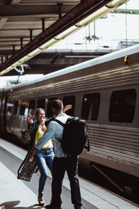 Cheerful couple embracing by train on railroad station platform