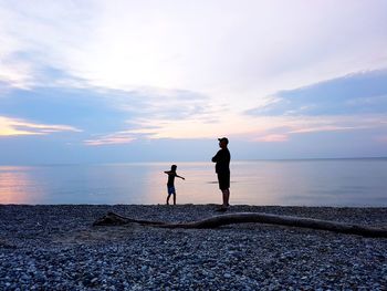 Father with son standing on shore at beach during sunset