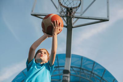 Low angle view of boy playing basketball against sky