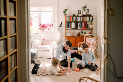 Father drawing with daughters while resting in living room at home