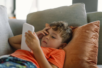 Young woman using mobile phone while lying on sofa at home