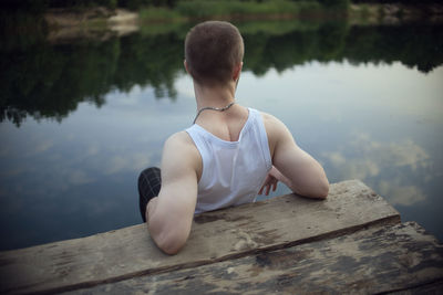Rear view of man sitting on lake against trees