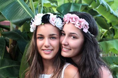 Portrait of smiling sisters wearing flowers against trees