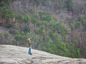 Full length of woman standing on rock against forest