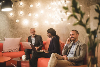 Male entrepreneur talking on mobile phone while sitting with colleagues in office