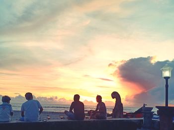 People sitting by sea against sky during sunset