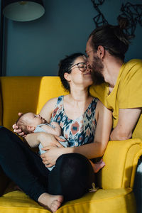 Woman sitting on yellow sofa at home holding her new born baby