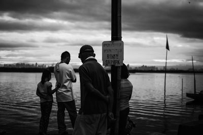 Rear view of men standing by river against sky