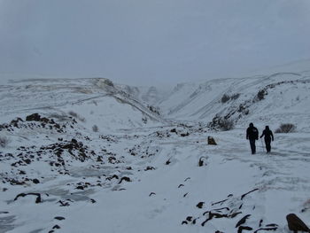 People on snow covered landscape against sky