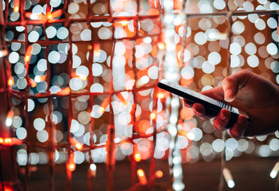 Close-up of hand holding smart phone against illuminated lighting decor at night