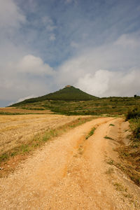 Dirt road amidst field against sky