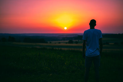 Rear view of man standing on field during sunset