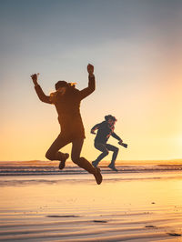 Friends jumping at beach against clear sky during sunset