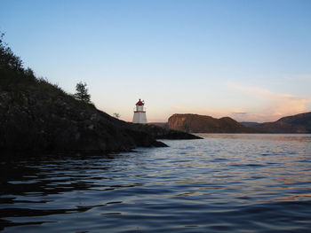 Lighthouse amidst sea and buildings against sky