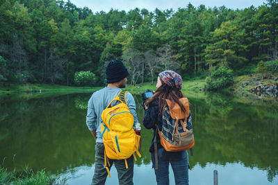 Rear view of women standing by lake against trees