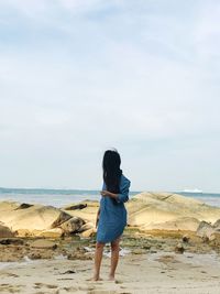 Woman with long hair standing at beach against sky