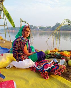 Woman sitting by river against sky