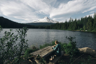 A young woman eats lunch at picnic table next to a lake near mt. hood.