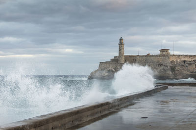 Sea waves splashing on shore against sky