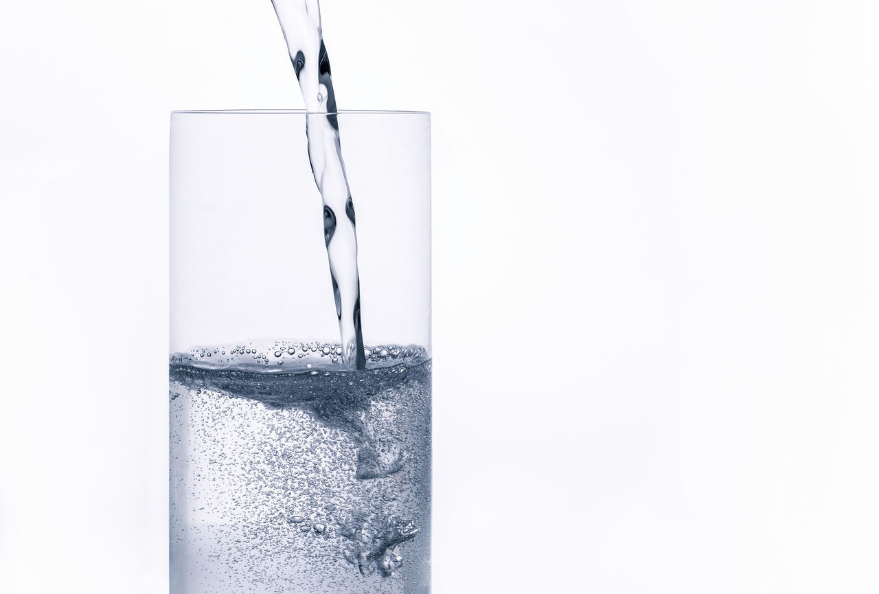CLOSE-UP OF GLASS POURING WATER WITH WHITE BACKGROUND