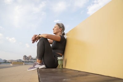 Thoughtful mature woman sitting with water bottle on bench