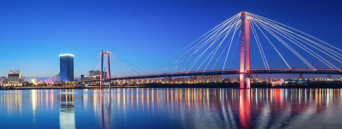 Illuminated suspension bridge over river against sky