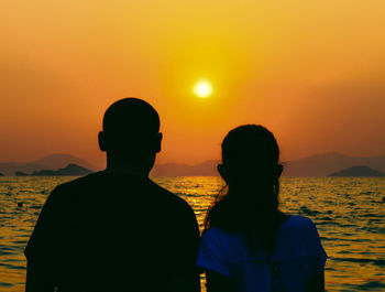 Rear view of people on sea against sky during sunset