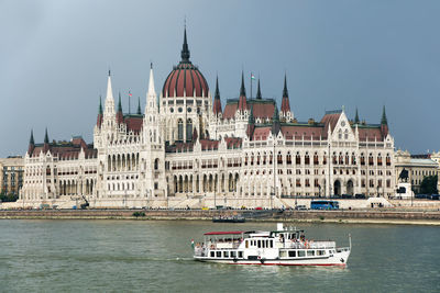 Hungarian parliament building by danube river against sky in city