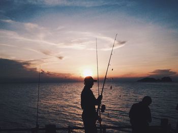 Silhouette people fishing by sea during sunset