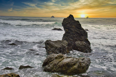 Rock formation on beach against sky during sunset