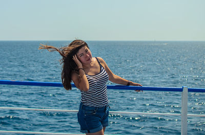 Full length of young woman standing by railing against sea