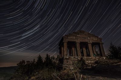 Low angle view of built structure against star trails at night
