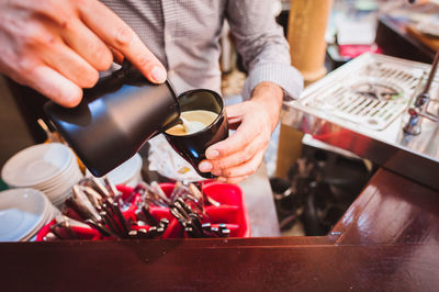 Midsection of barista pouring coffee in cup from container at cafe