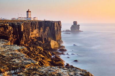 Rock formation by sea against sky during sunset