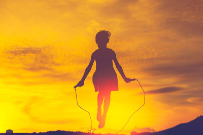 Silhouette girl jumping rope against orange sky