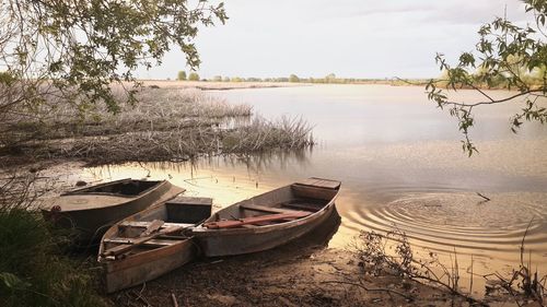 Boats moored on shore by lake against sky