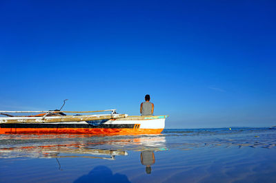 Boats in calm sea against clear blue sky