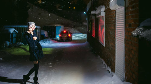 Full length of young woman smoking cigarette during snowfall at night