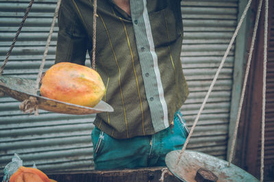 Midsection of man holding papaya on weight scale at market