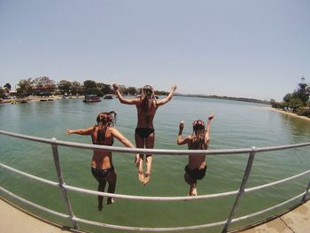 Rear view of women jumping in lake against clear sky