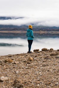 Unrecognizable woman walking by the lake wearing a jacket with her hands in her pockets