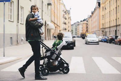 Father crossing road with children while pushing baby stroller in city