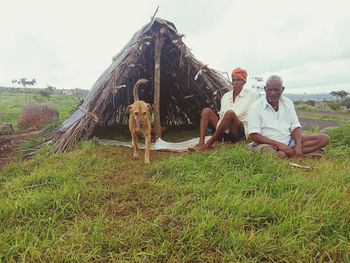 People sitting on field by land against sky