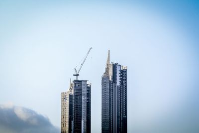 Low angle view of crane by buildings against sky