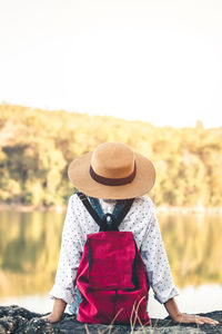 Rear view of woman with hat sitting against sky