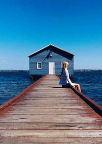 Rear view of woman on pier over sea against clear blue sky