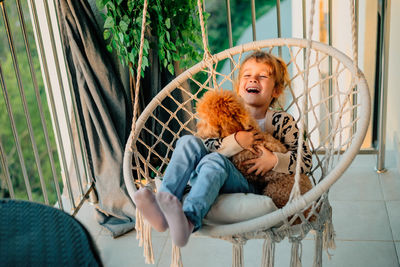 Happy little girl, child hugging with a smile her pet, poodle dog at home on the balcony in spring