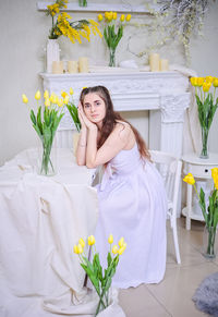 A beautiful young girl in a white dress and with long wavy hair against a background of yellow tulip