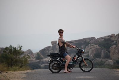 Side view of smiling young man on motor scooter over road