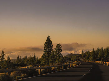 Road by trees against sky during sunset